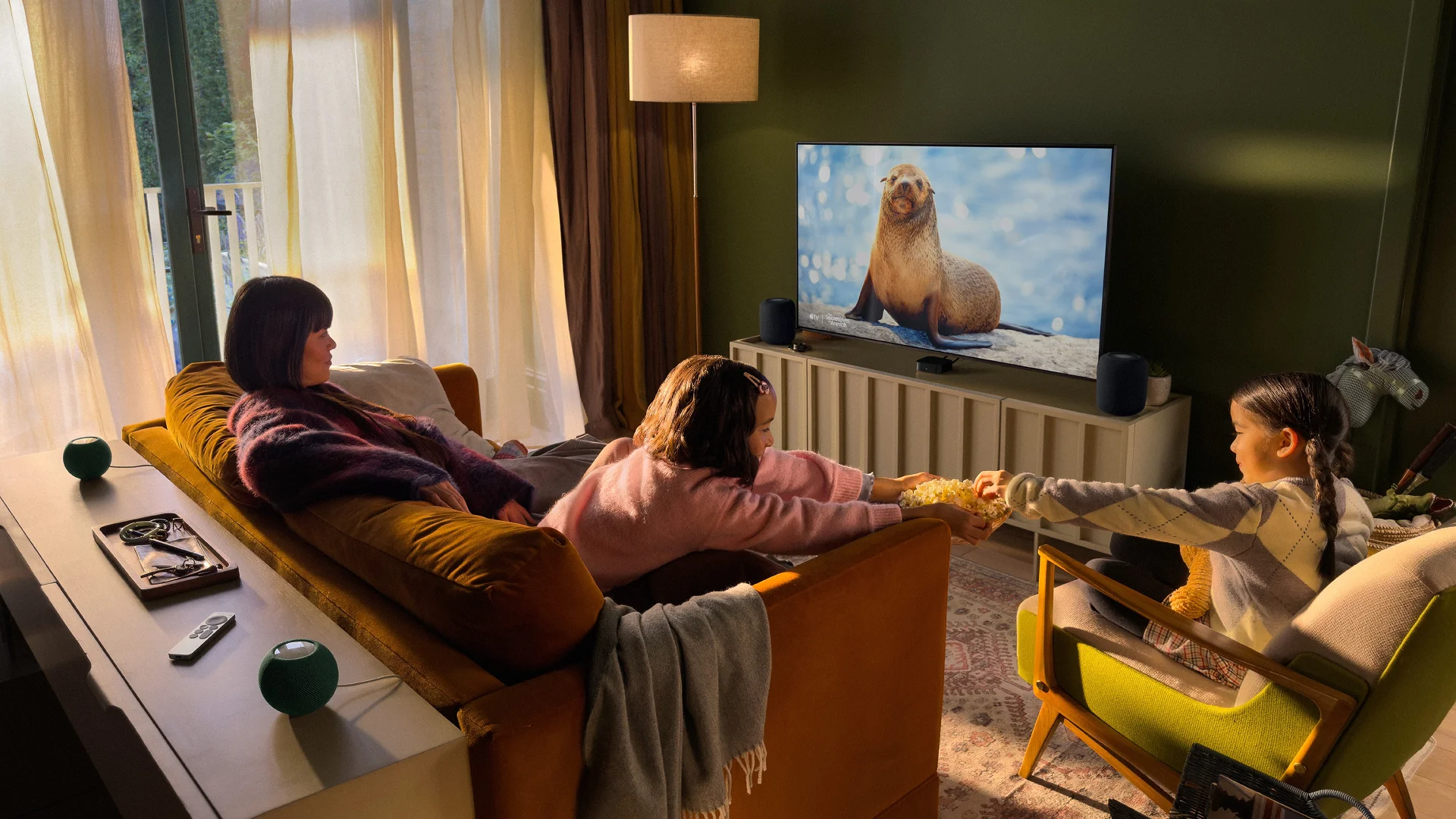 Porodica gleda televiziju uz Apple TV 4K, dva HomePod i dva HomePod mini 2 zvučnika