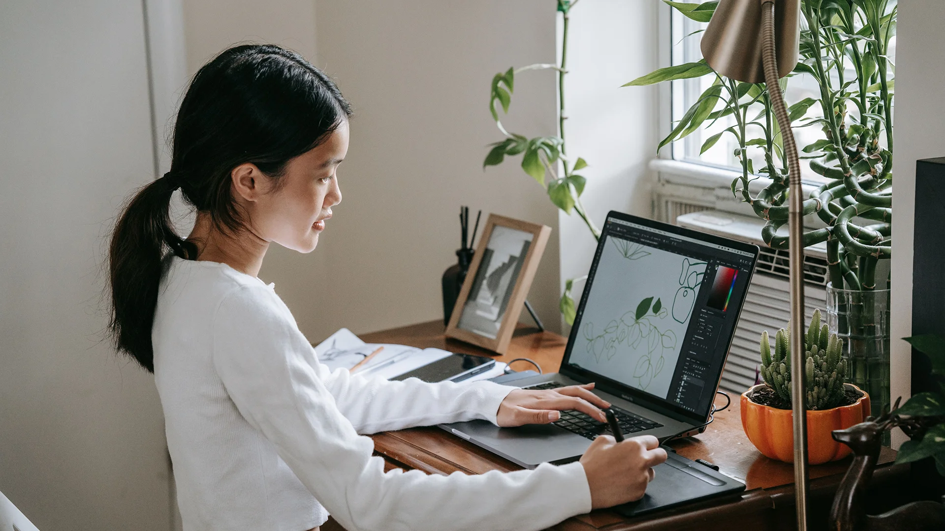 Designer working on a laptop with creative software while using a graphics tablet and stylus