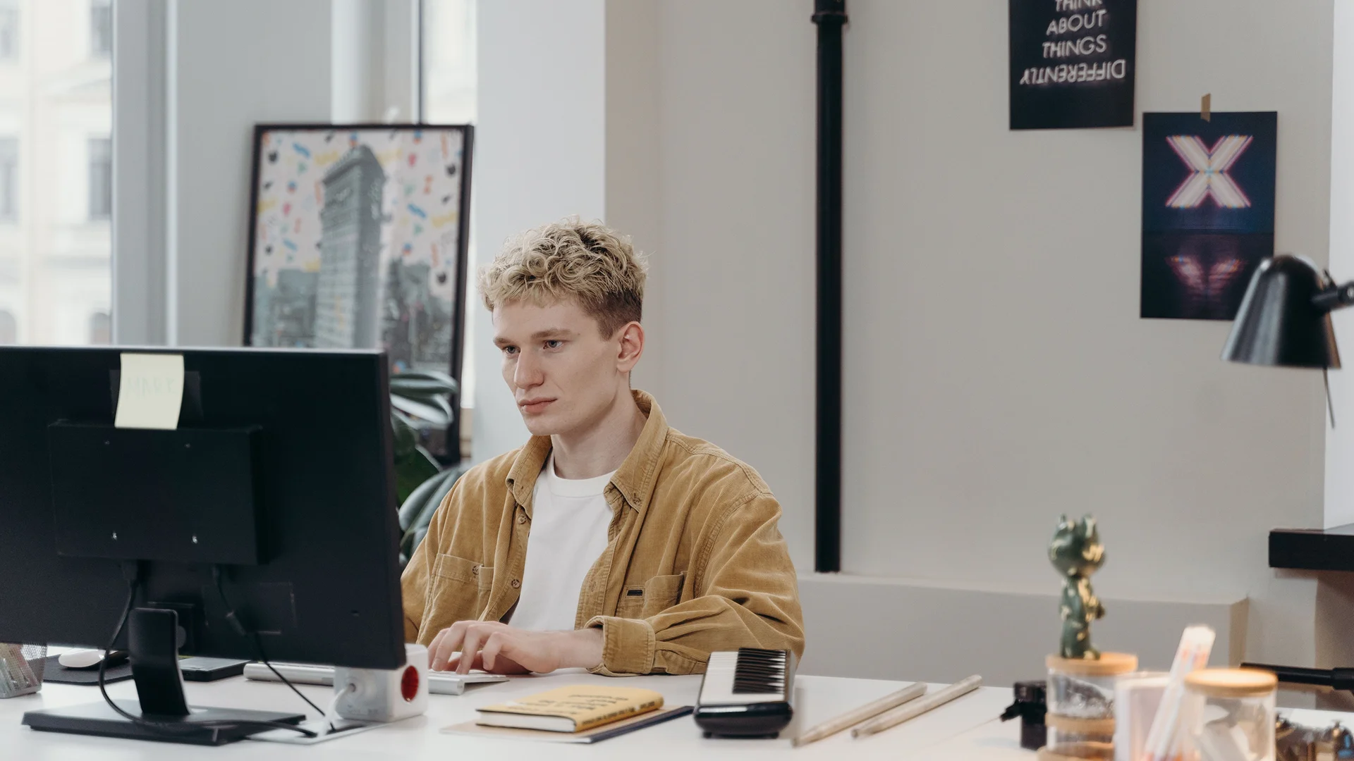 An employee works at a desktop computer in an office, with a monitor, keyboard and notebook on the desk